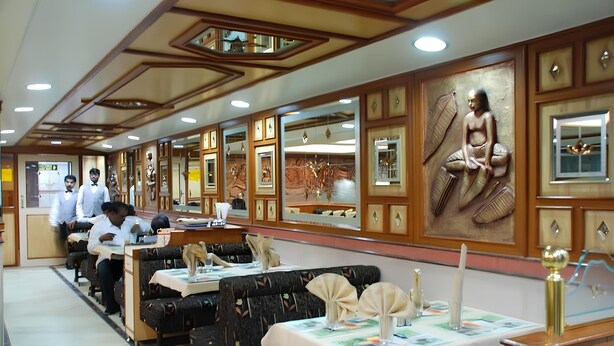 Un restaurant aux murs lambrissés, orné de tableaux encadrés, et dont les tables sont dressées avec des nappes blanches et des bougies.