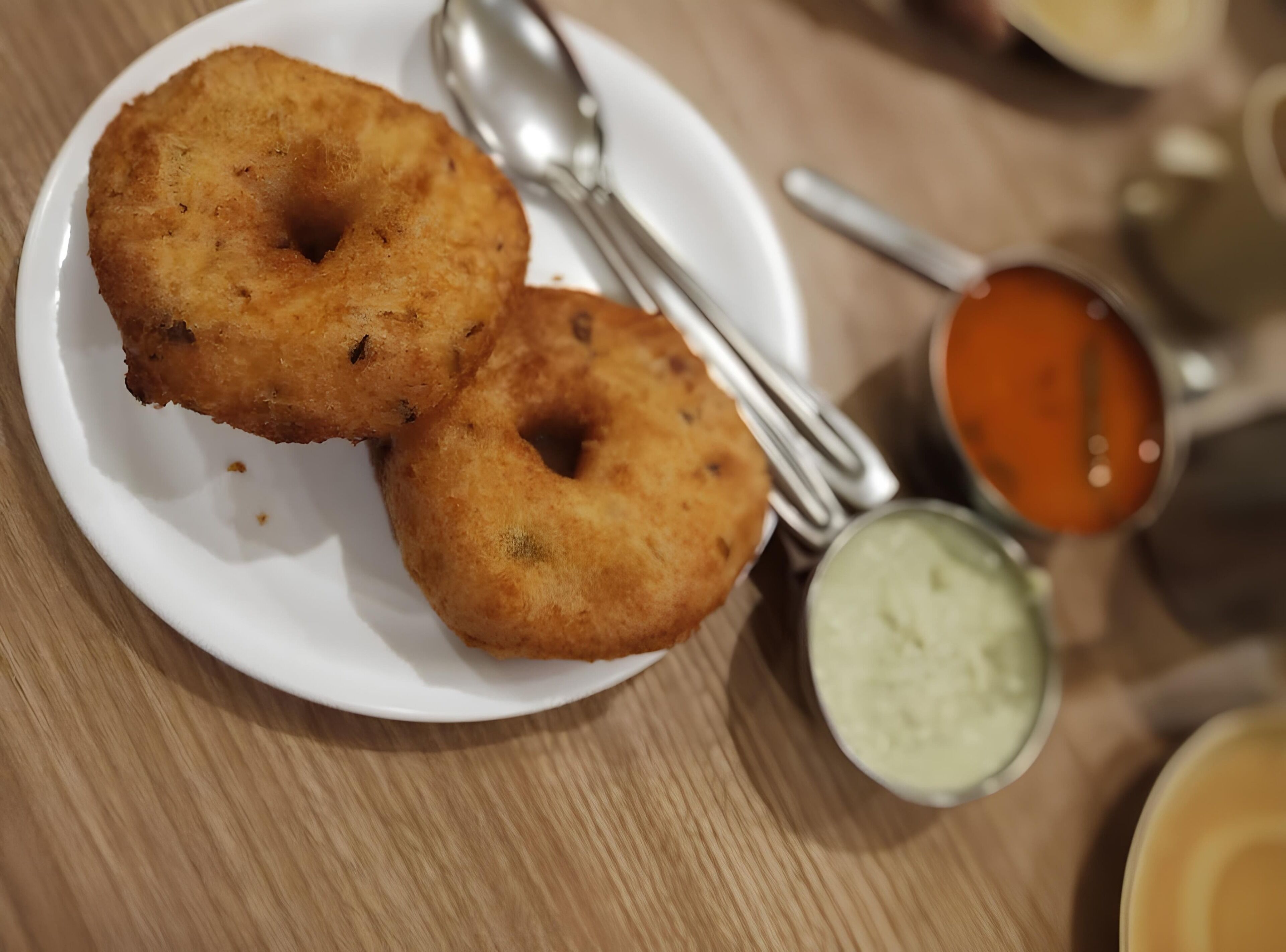 A plate with two fried dough items and two spoons, one with a red sauce and one with a green sauce.