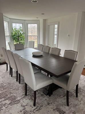Une salle à manger avec une table rectangulaire, six chaises, une plante en pot et de grandes fenêtres.