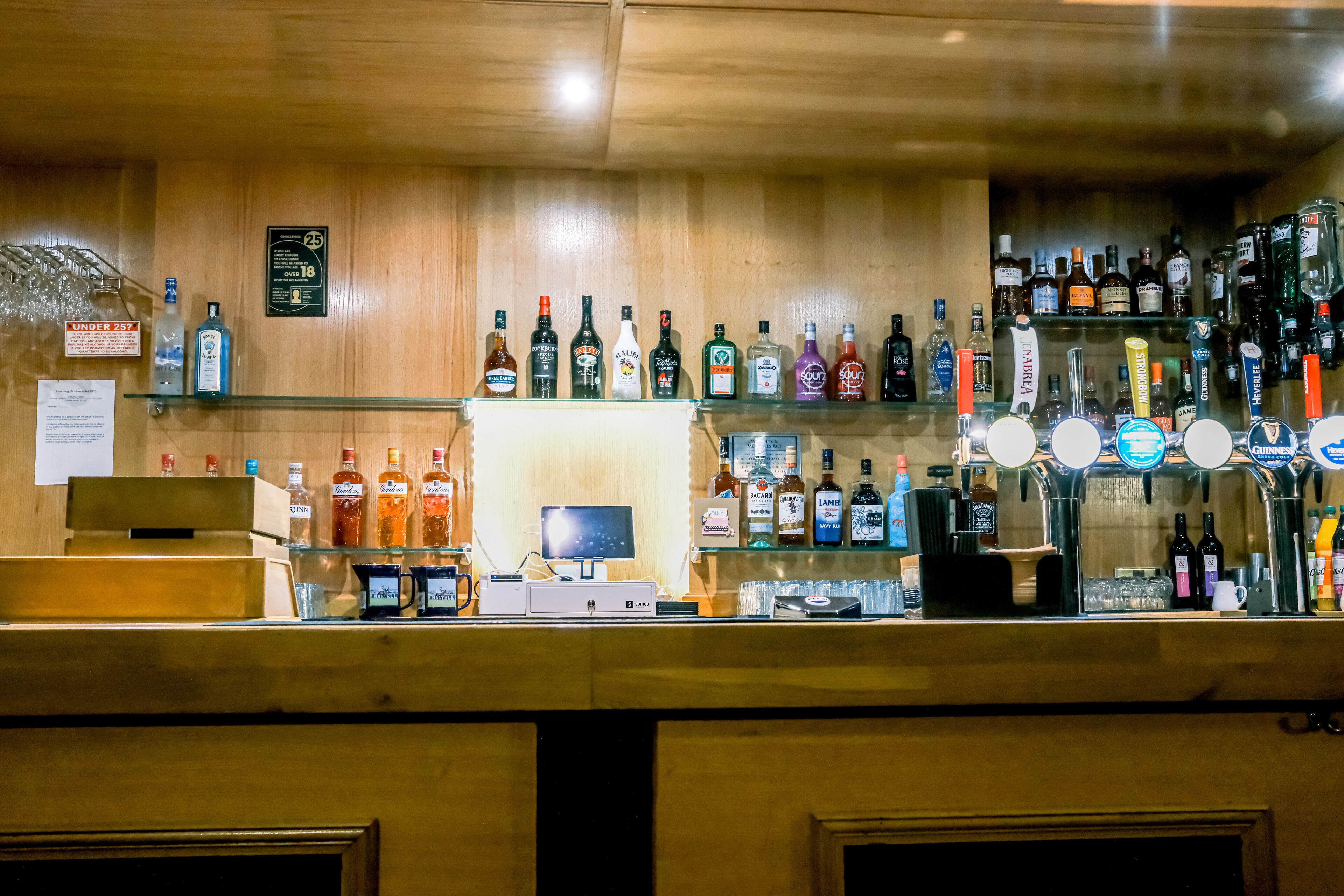 A bar area with shelves of liquor bottles, a cash register, and a computer monitor.