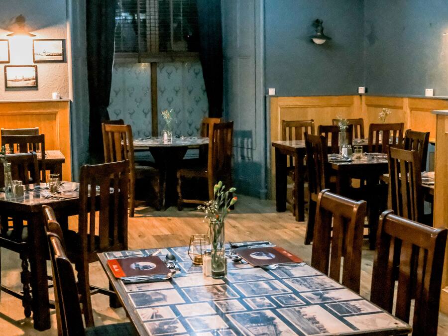 Un comedor con mesas y sillas de madera, un mantel estampado y un jarrón con flores.