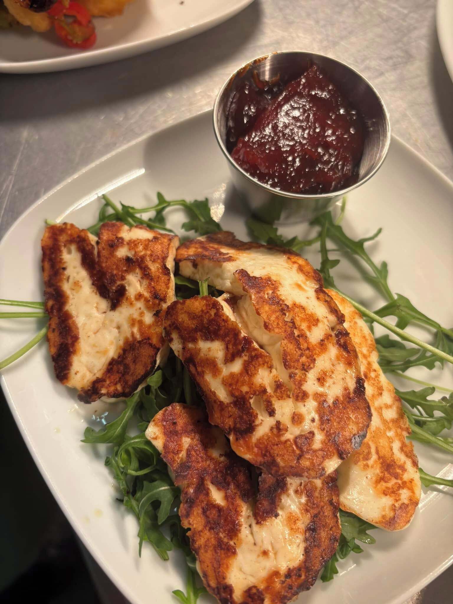 A plate with grilled chicken breast, arugula, and a small bowl of sauce.