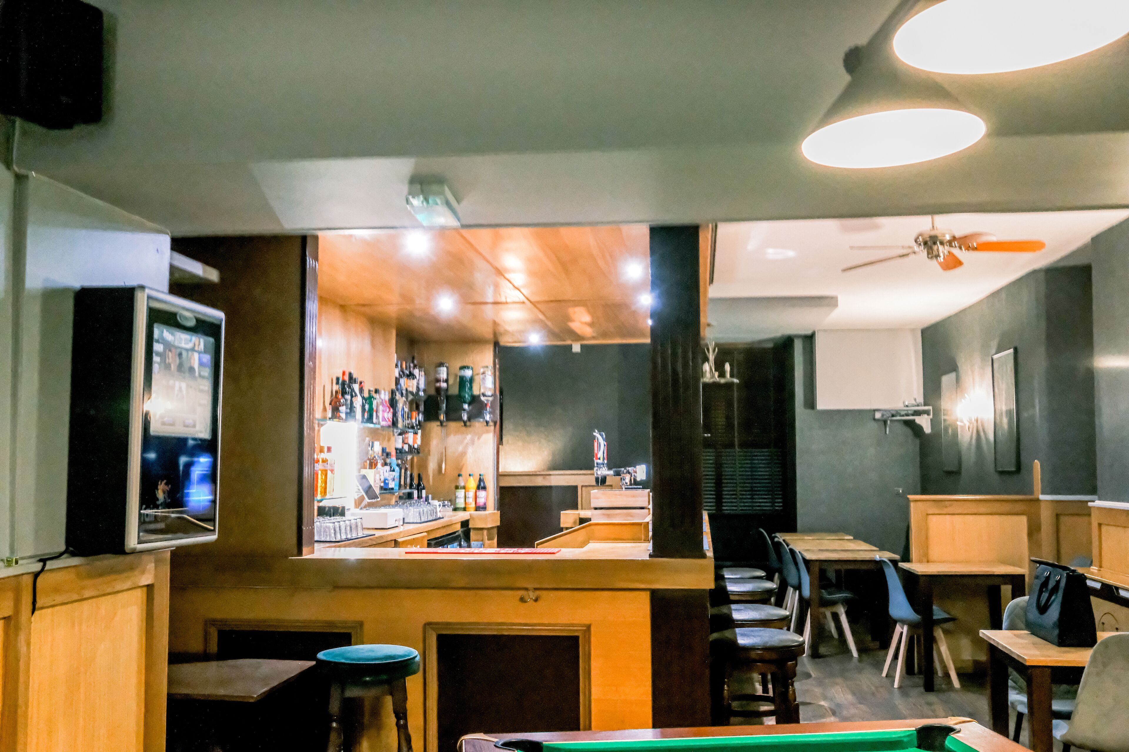 Un área de bar con mesa de billar, taburetes y una pantalla de televisión.