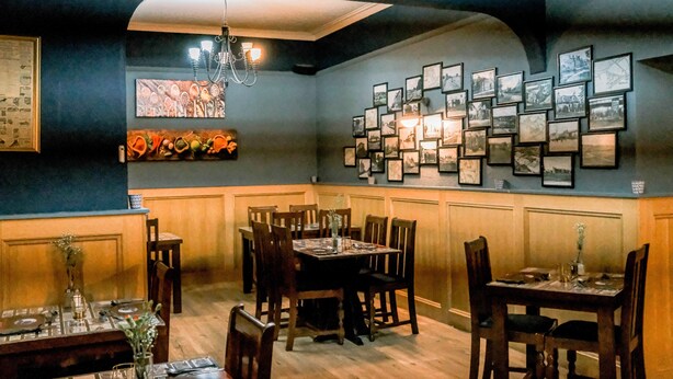 A dining area with wooden tables and chairs, a chandelier, and a wall decorated with framed pictures. - Hillside Hotel & Restaurant (Montrose)