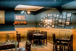 A dining area with wooden tables and chairs, a chandelier, and a wall decorated with framed pictures. - Hillside Hotel & Restaurant (Montrose)