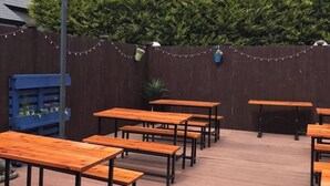 An outdoor patio with wooden tables and benches, a wooden fence, and string lights. - Hillside Hotel & Restaurant (Montrose)