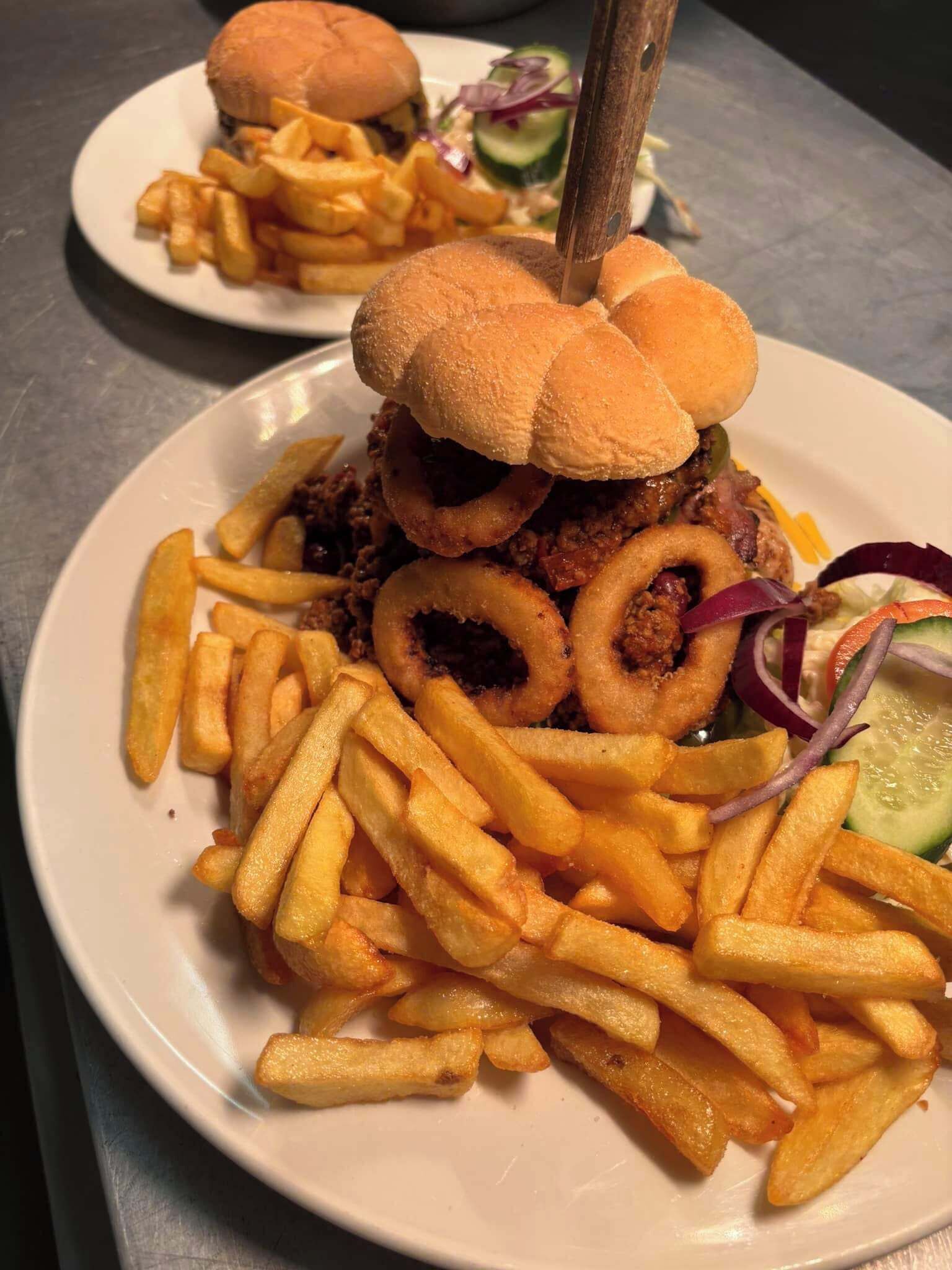 Un plato con una hamburguesa, aros de cebolla y papas fritas.