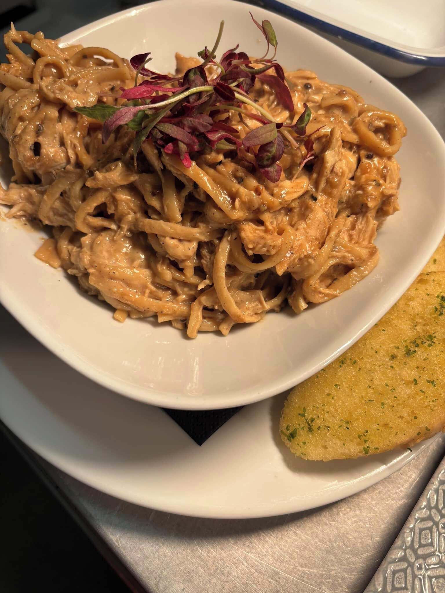 Plat de pasta amb salsa cremosa i una porció de pa.