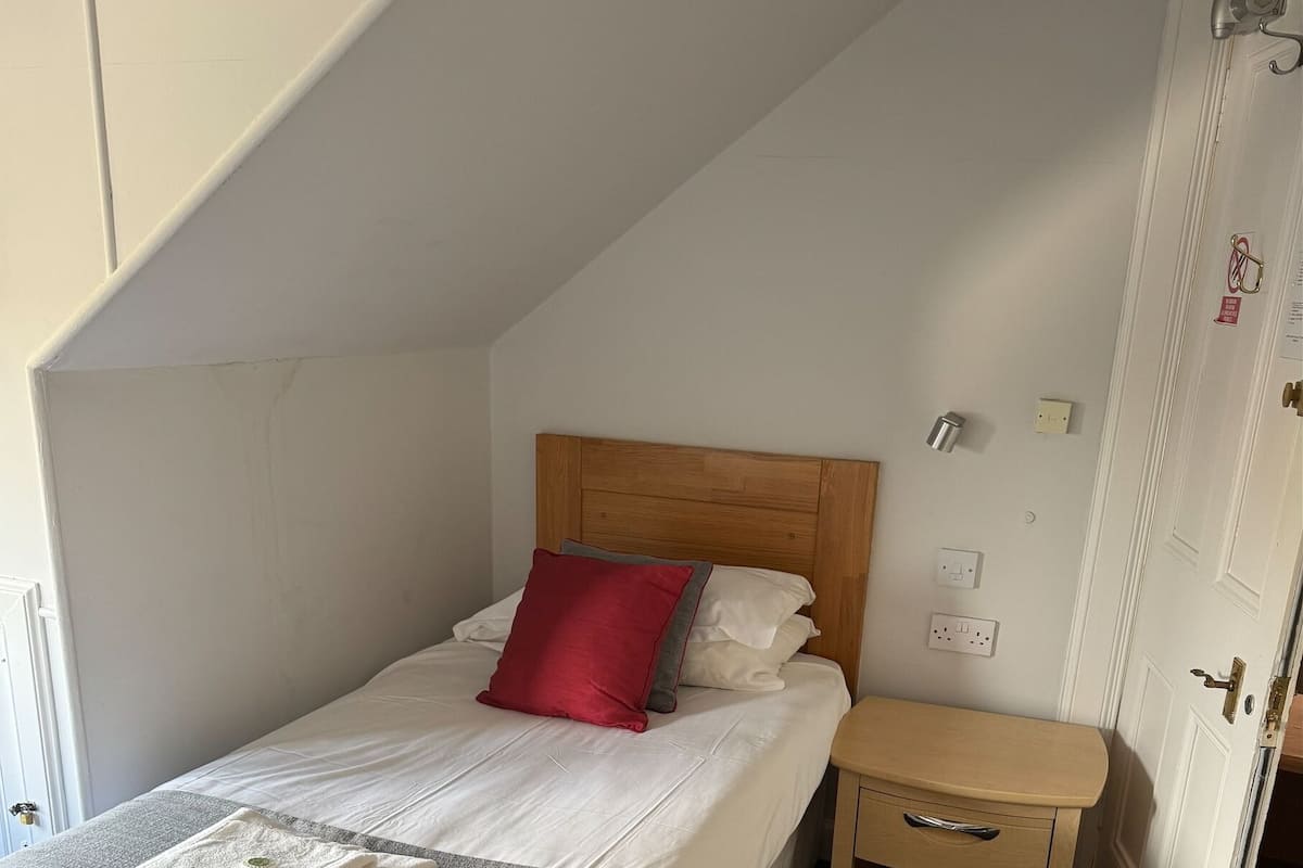 A neatly made bed with a red pillow, a bedside table, and a door.