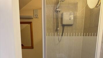 Un baño con ducha acristalada, inodoro y espejo en la pared.