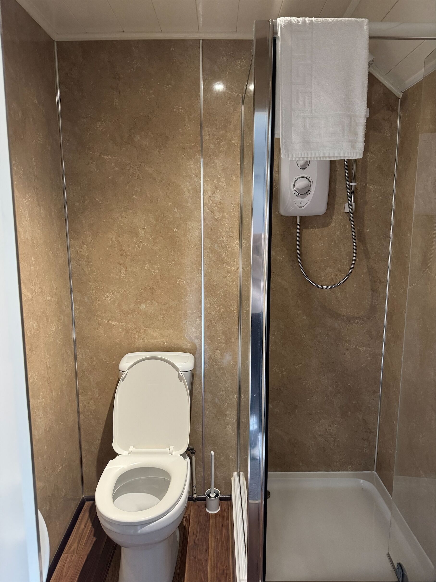 A bathroom with a toilet, a shower enclosure, and a towel hanging on a rack.