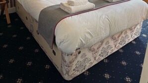 A neatly made bed with a wooden headboard, a bedside table with a lamp, and a patterned wall. - Hillside Hotel & Restaurant (Montrose)