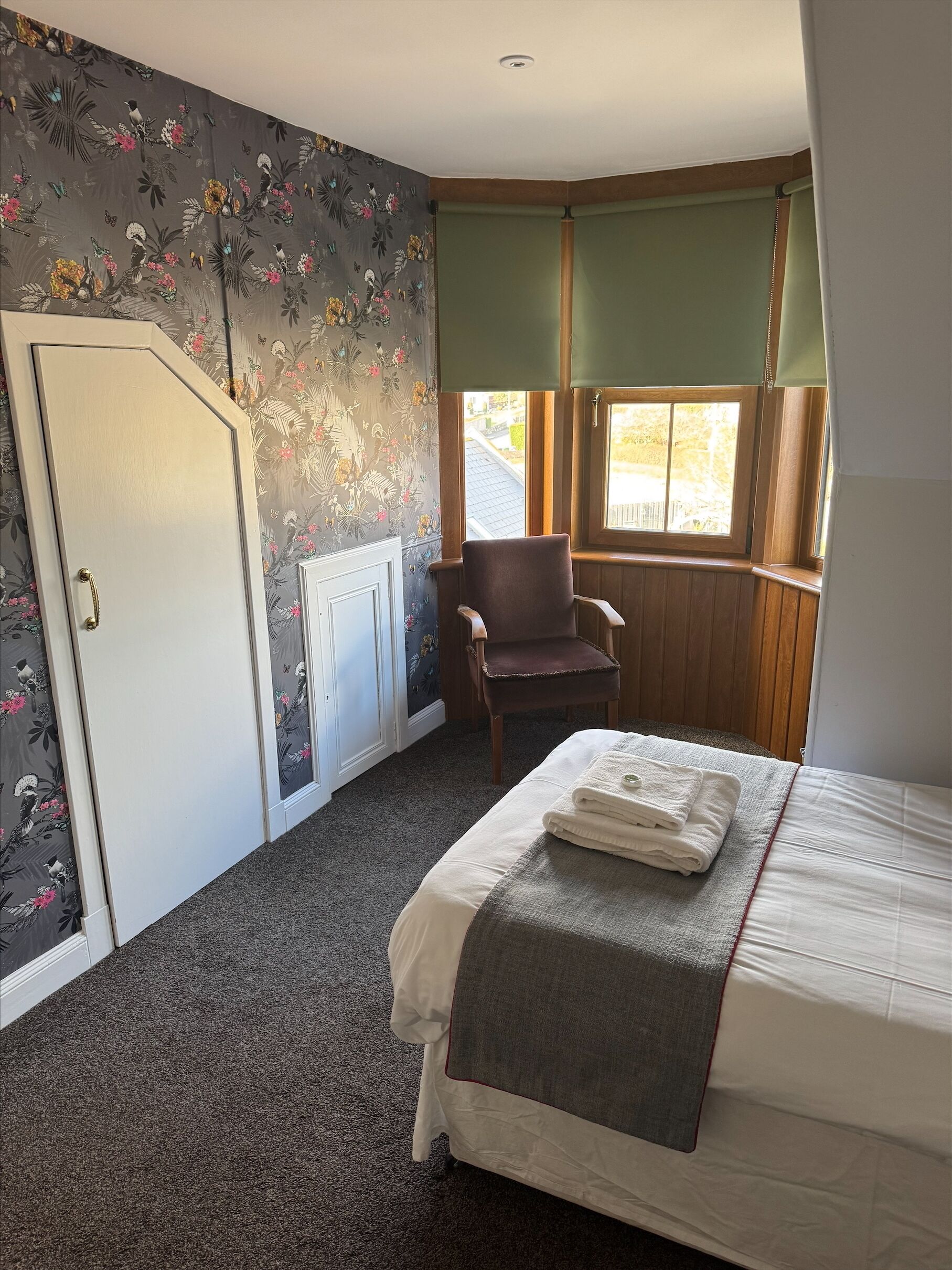 Un dormitorio con cama, una silla, un radiador y una ventana con cortinas.