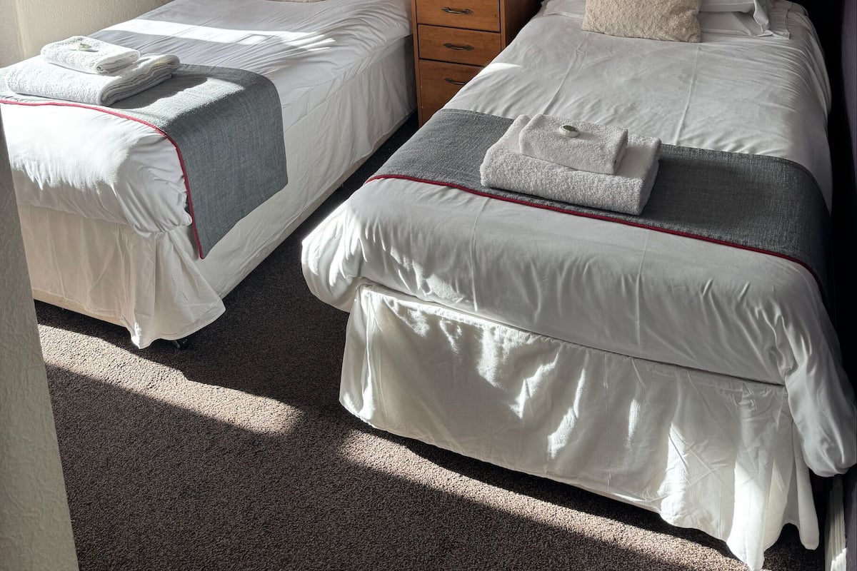 A hotel room with two beds, a wooden headboard, a nightstand, and a small table.