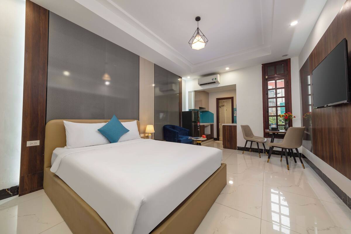 A hotel room with a large bed, a desk with two chairs, a television, and an air conditioning unit.