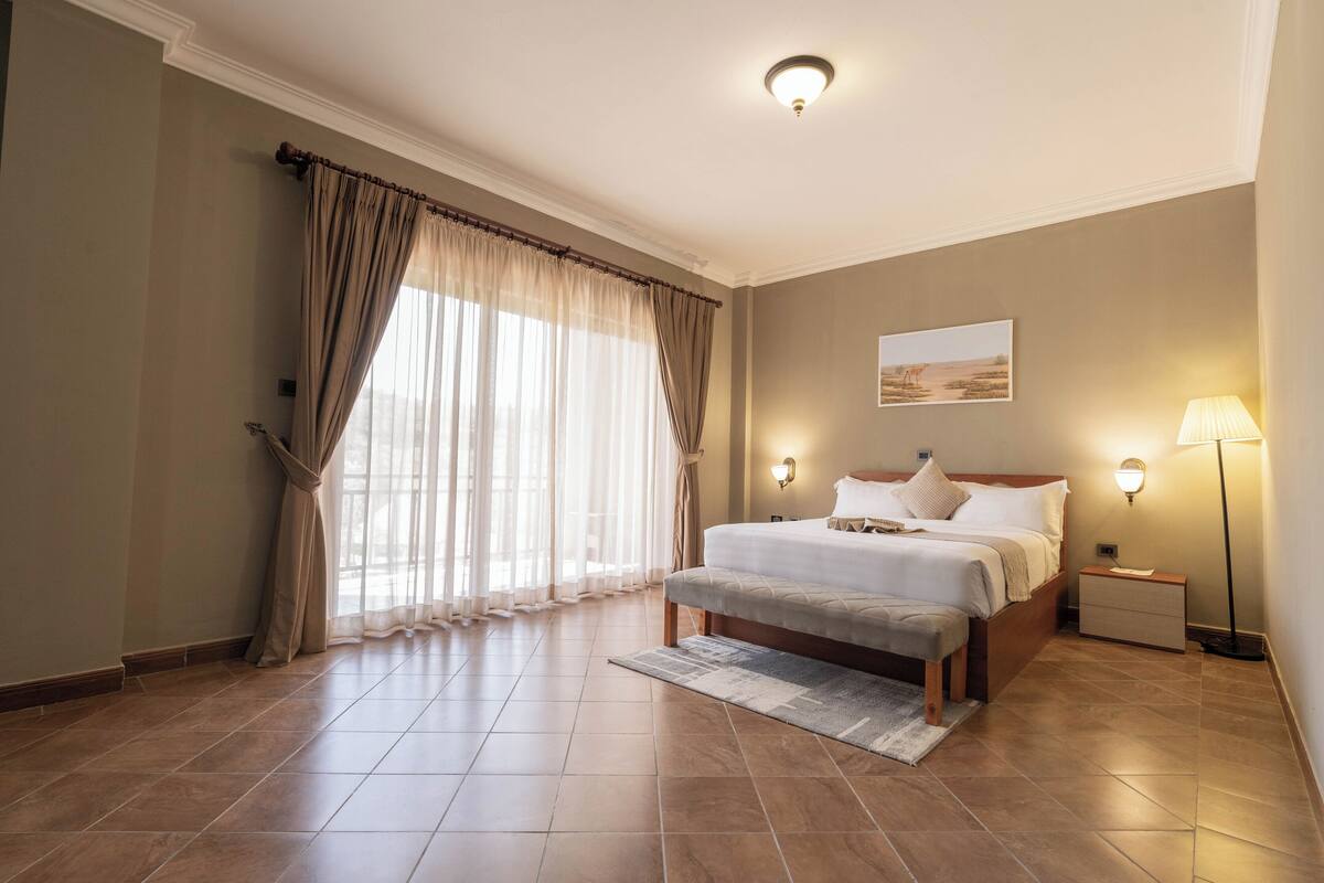 A bedroom with a large bed, bedside lamps, a nightstand, and a window with curtains.