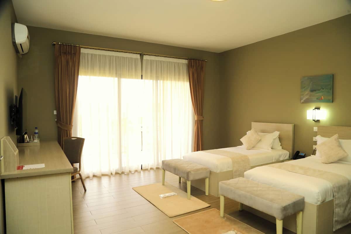 A hotel room with two beds, a desk, a chair, and a large window with curtains.