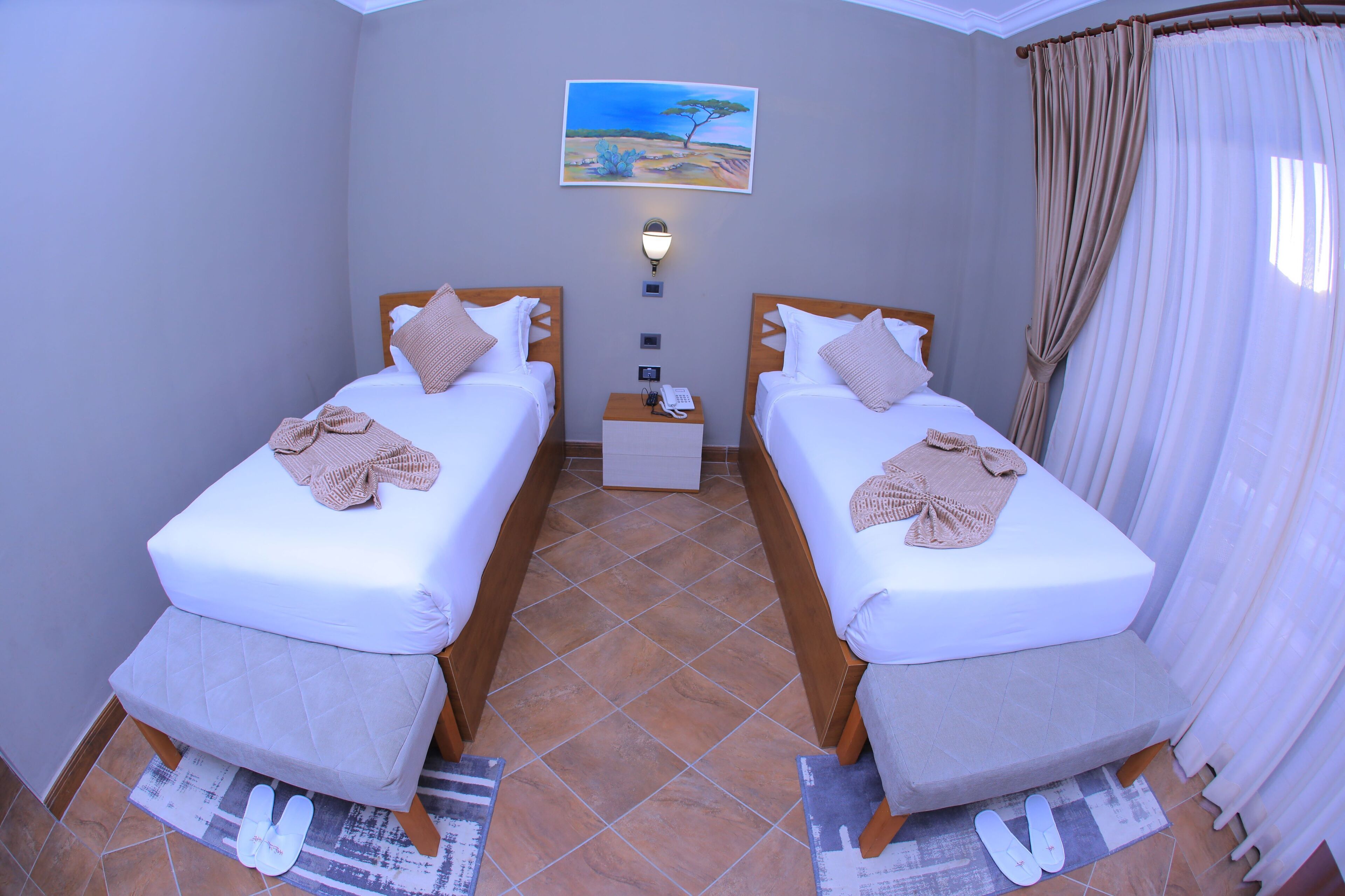 Quarto com duas camas, uma mesa de cabeceira, um quadro e uma janela com cortinas.