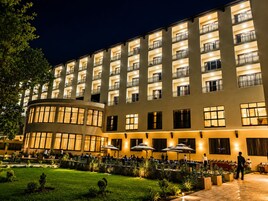 Un hotel con varios balcones, fachada de vidrio curva y una zona de estar al aire libre con sombrillas.