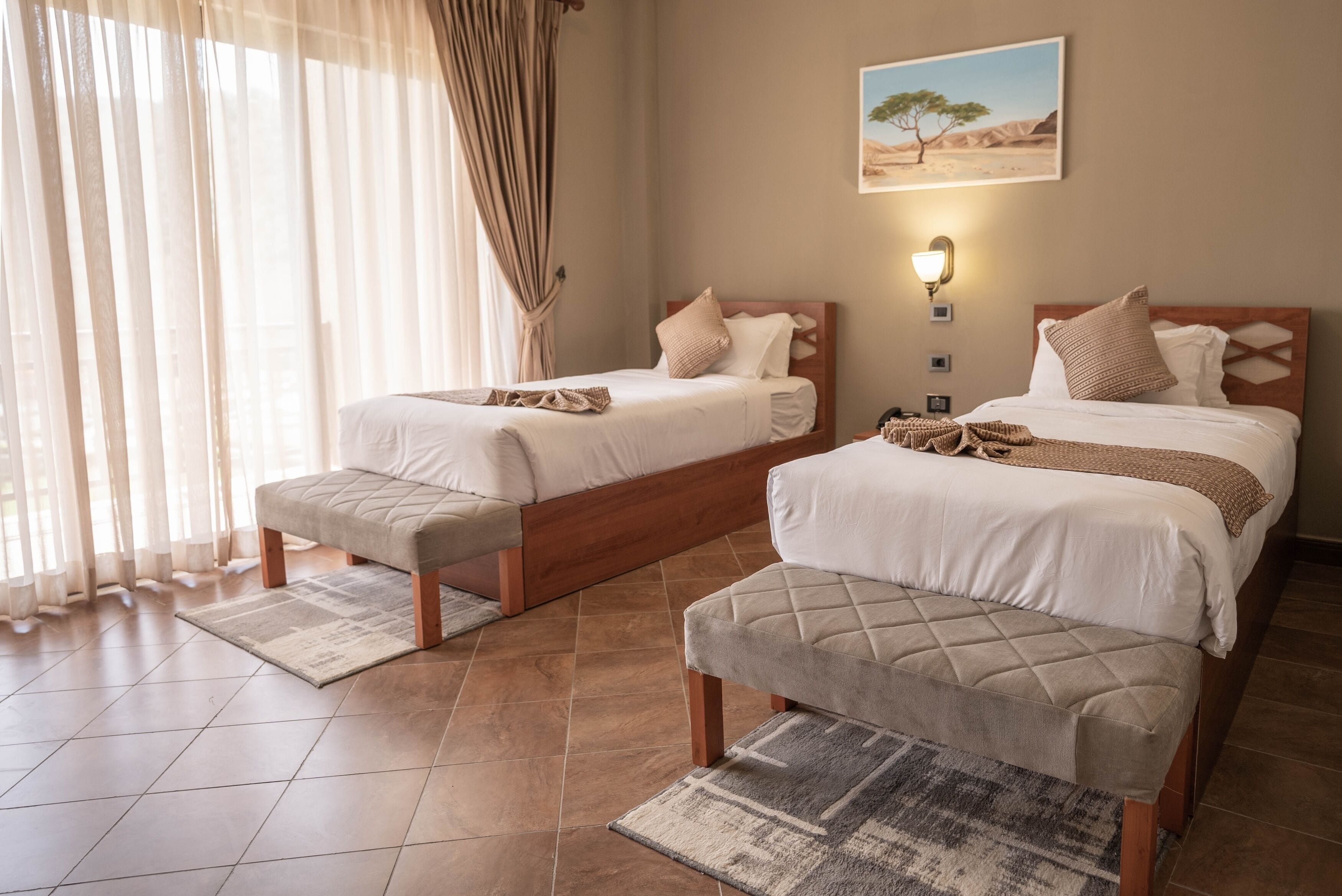 A hotel room with two beds, a bench, a rug, and a painting on the wall.