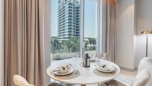 Zona pranzo con tavolo rotondo per due persone, vista su un grattacielo e balcone con palme.