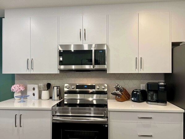 Cocina moderna con armarios blancos, electrodomésticos de acero inoxidable y una encimera con cafetera y tostadora.