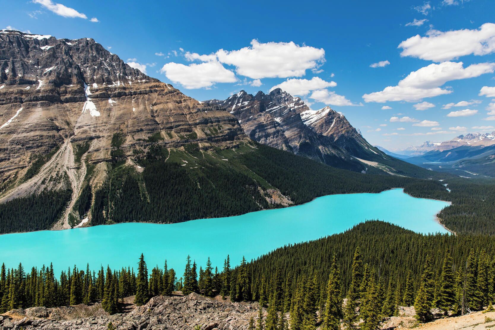 A mountain landscape with a turquoise lake surrounded by dense forests and rugged mountains.