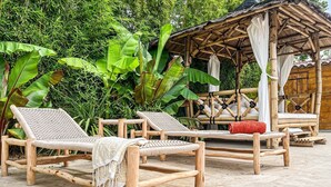 A wooden outdoor seating area with lounge chairs and a bamboo structure.
