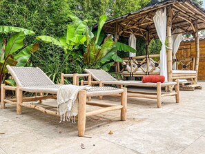 Uma área de estar ao ar livre com cadeiras de descanso e estrutura de bambu.