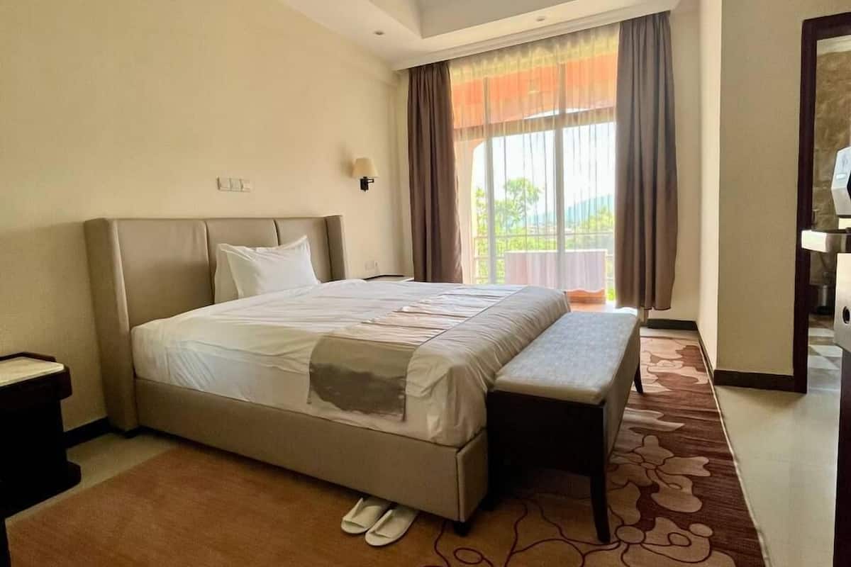 Habitación de hotel con una cama grande, una banca, una mesita de noche y vistas al exterior a través de una ventana.