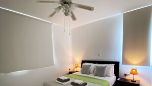 A modern bedroom with a bed, two bedside tables, a ceiling fan, and a large window. - 70 PAP - Stay Anthea Gardens - Calm Living (Ayia Marinouda)