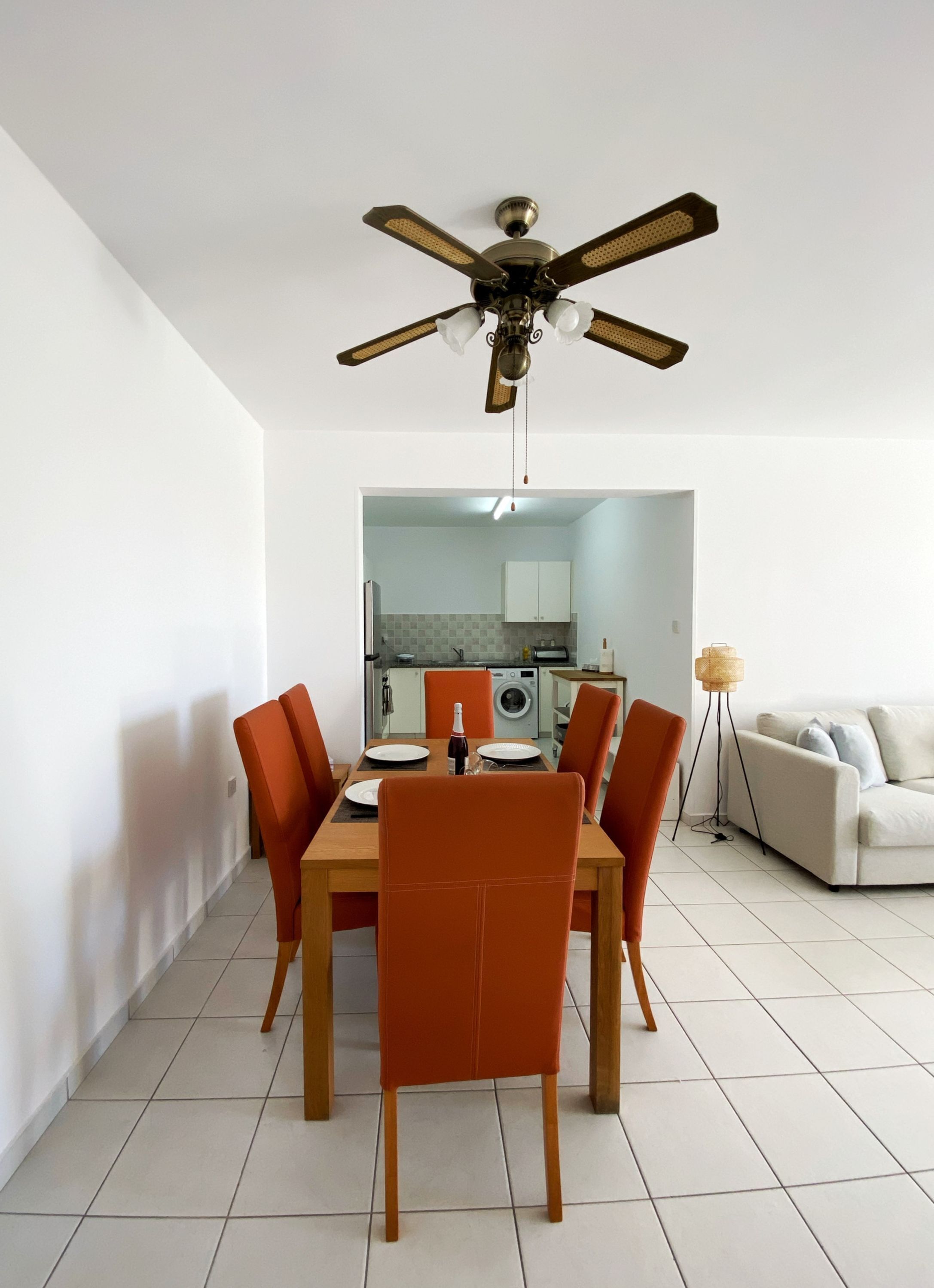 A dining area with a table and chairs, a ceiling fan, and a kitchen in the background.