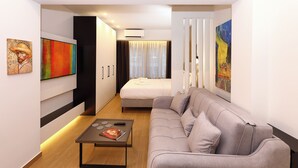 A modern hotel room with a bed, a grey sofa, a small table with a magazine, and artwork on the walls.