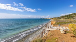 Una playa costera con un paseo de madera y escalones de piedra que conducen a una plataforma de observación.
