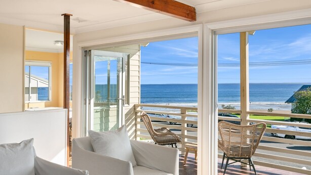 A balcony with wicker chairs, a white sofa, and a view of the ocean. - Gerroa House located mere steps from Seven Mile Beach. (Gerroa)