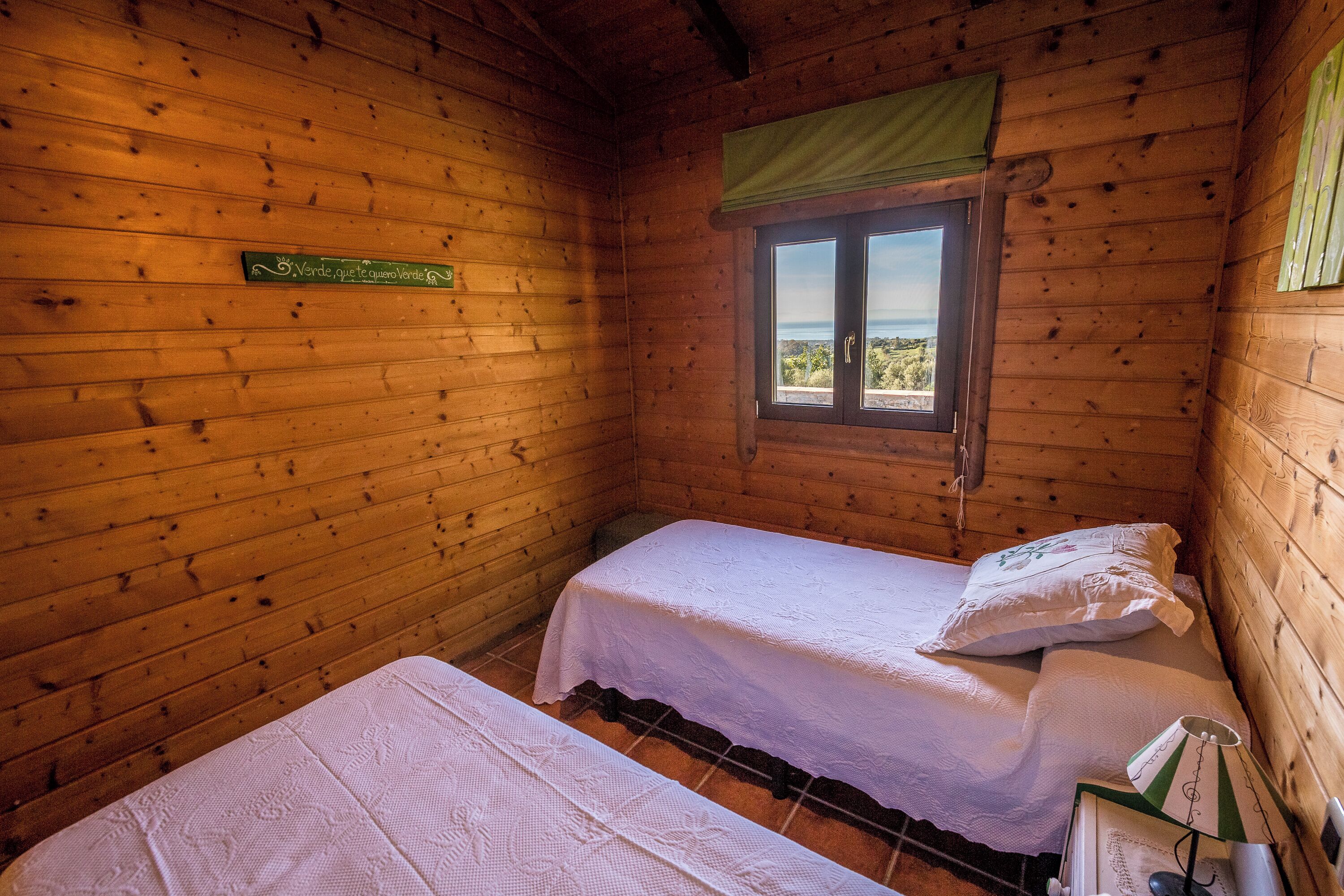 Une chambre de style cabane en bois avec deux lits, une fenêtre donnant sur un paysage agréable et un panneau vert sur le mur.