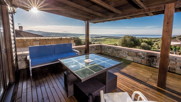 Un patio al aire libre con una mesa de vidrio, sofá azul, sillas de mimbre y un muro de piedra de fondo.