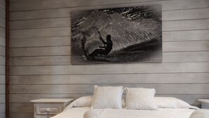 Un dormitorio con cama, almohadas y una obra de arte colgada en la pared de un surfista.