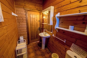 A wooden-paneled bathroom with a sink, mirror, shelves, and a sign in Spanish. - Viviendas Rurales Las Cabañas (Tarifa)