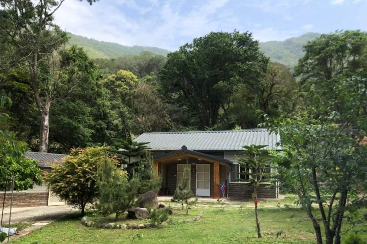 A house with a sloped roof, surrounded by a well-maintained garden with various plants and trees.