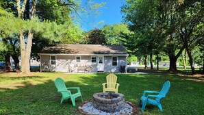 A house with a backyard containing a fire pit and two Adirondack chairs.