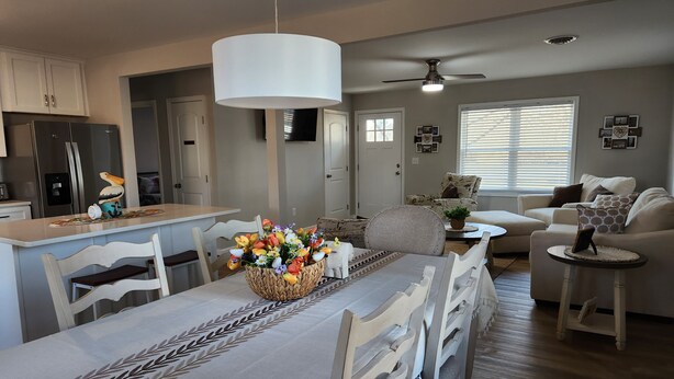 A modern kitchen with a central island, dining area with a table set for four, and a living room with a sofa and a coffee table.