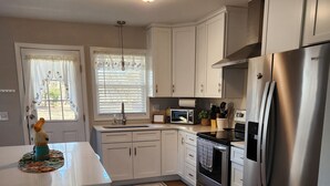 A modern kitchen with white cabinets, stainless steel appliances, and a wooden floor.