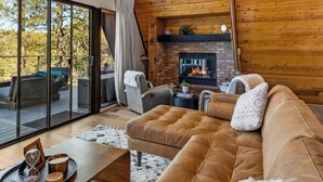 A cozy living room with a large brown sectional sofa, a wooden ceiling fan, and a fireplace. - Kachina A-Frame Hideaway | AC | Hot Tub | Firepit (Flagstaff)