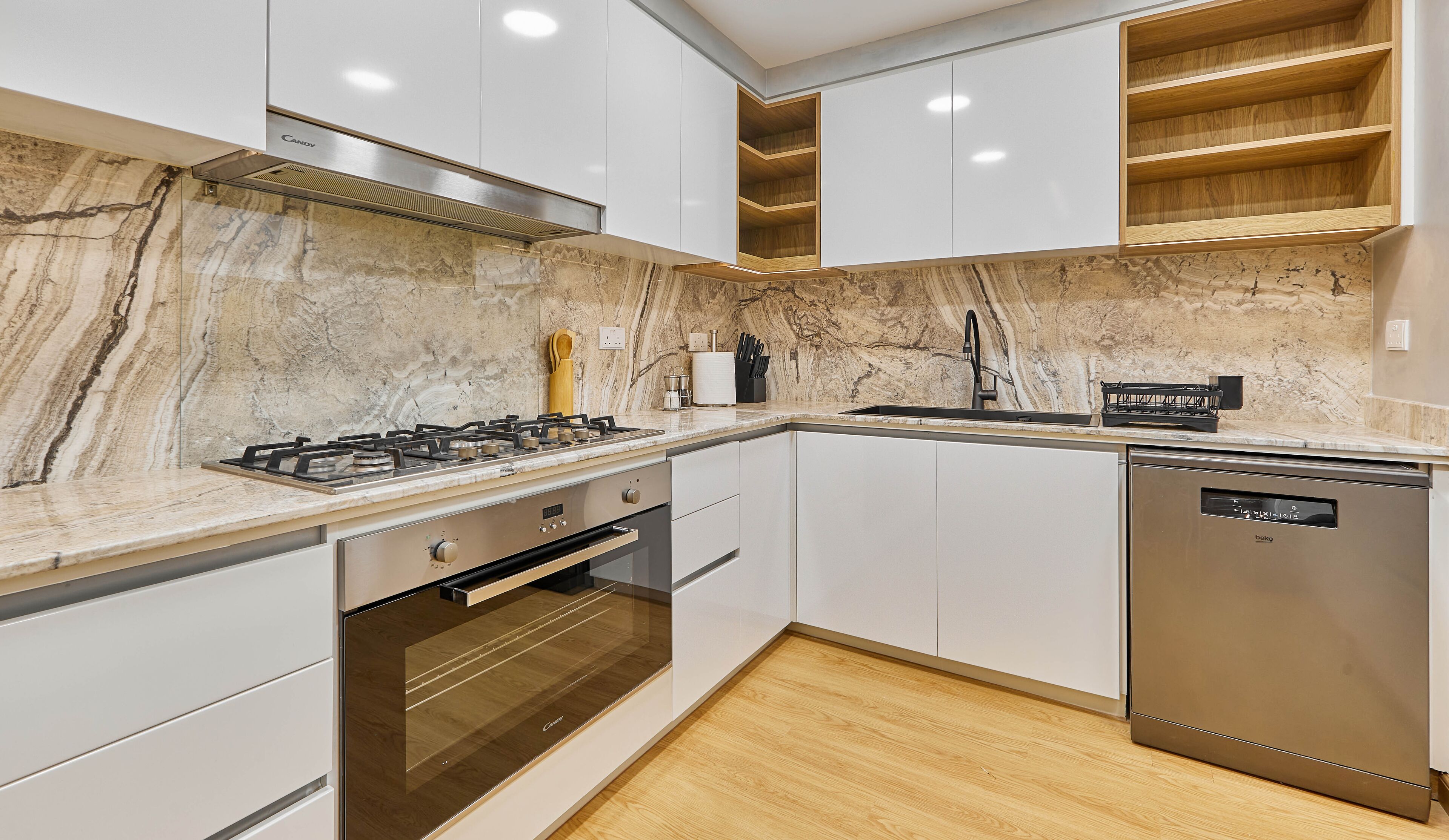 A modern kitchen with white cabinets, a marble backsplash, a built-in oven, a dishwasher, and a wooden shelf.