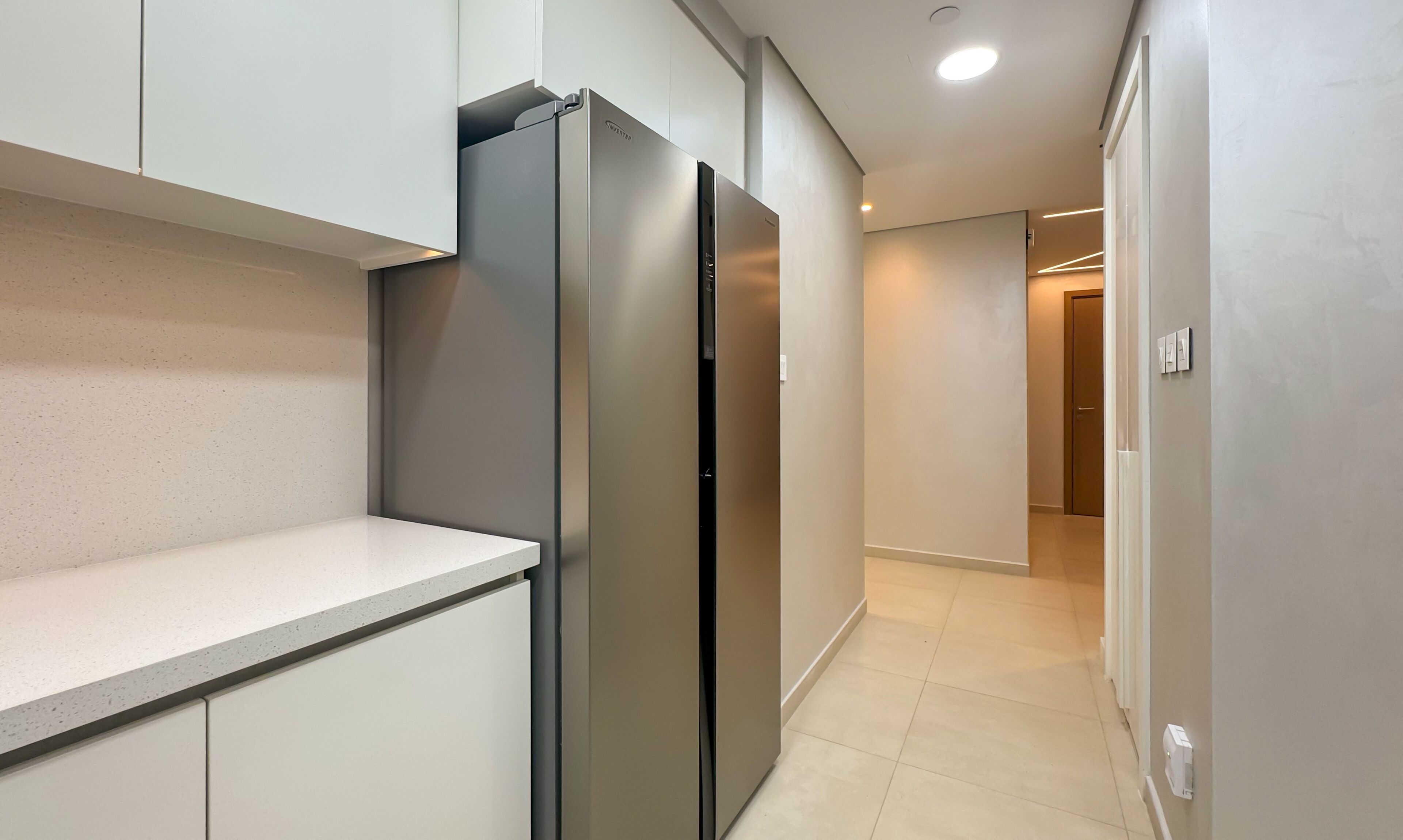 Una cocina moderna con electrodomésticos de acero inoxidable, una encimera blanca y un pasillo que lleva a una puerta.