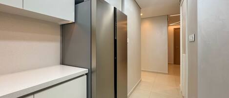 Una cocina moderna con electrodomésticos de acero inoxidable, una encimera blanca y un pasillo que lleva a una puerta.