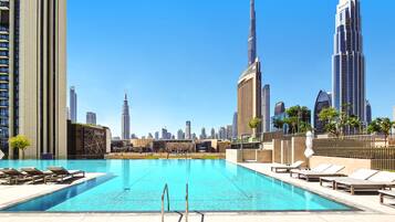 A swimming pool with lounge chairs, surrounded by high-rise buildings, including the Burj Khalifa.