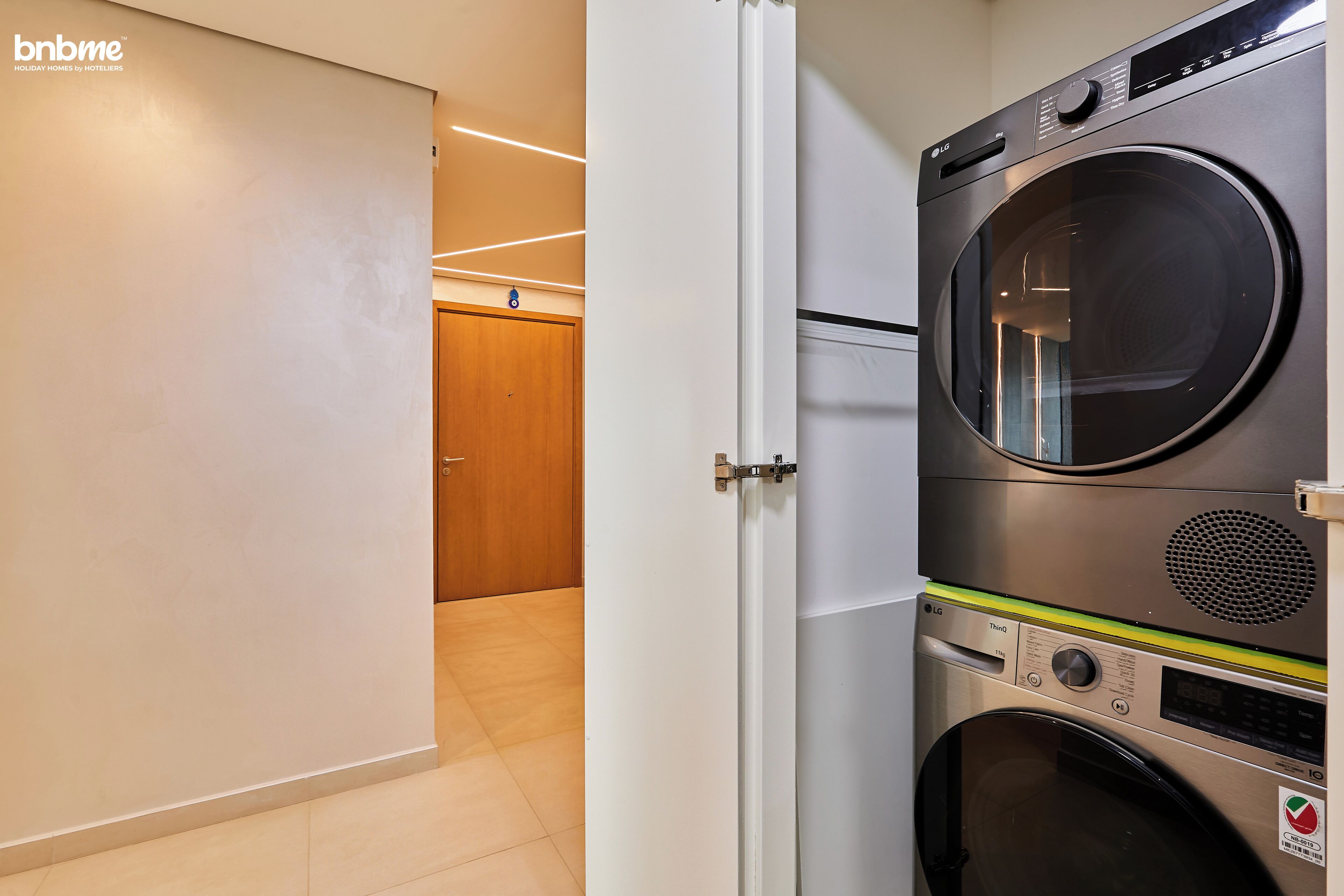 Habitación de hotel con diseño moderno, que incluye lavadora y secadora, una puerta de madera y piso de baldosas.