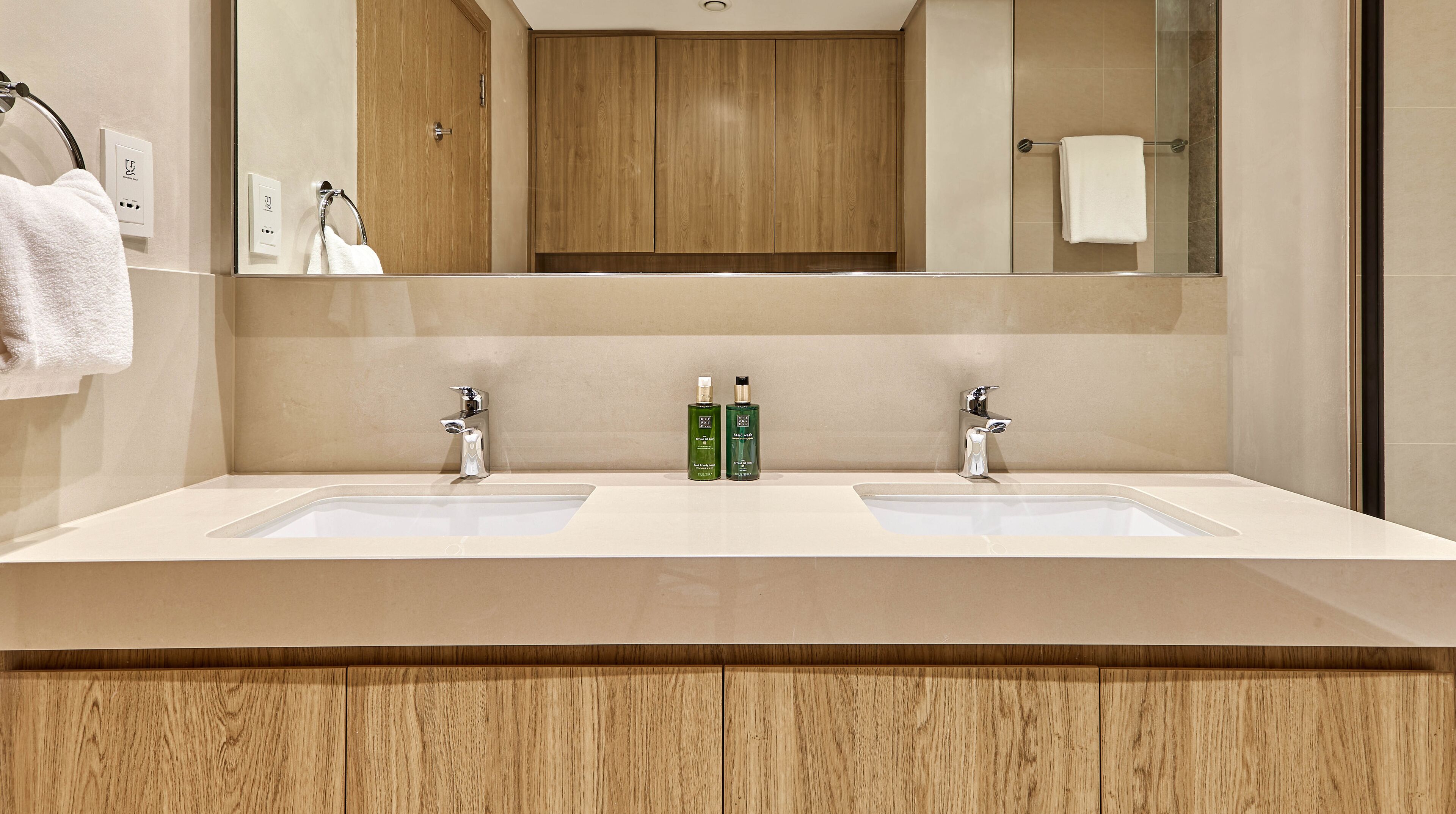 Un baño moderno con dos lavamanos, armarios de madera y un espejo grande.